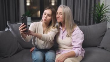 Torun ve büyükanne oturma odasında oturan akıllı telefondan fotoğraflara bakarlar. Aile günü, olumlu duygular..