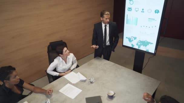 Üzleti találkozó hivatalban, fiatal üzletember beszél egy találkozón, és bemutatja a pénzügyi infografika a konferenciateremben, férfi öltönyben kommunikál kollégáival, infografika a TV képernyőn. — Stock videók