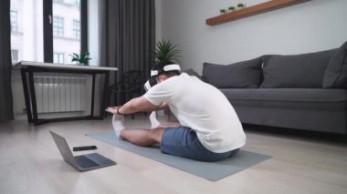 Sanal gerçeklik gözlüklü genç adam kaslarını esnetiyor, spor yapıyor, modern teknolojiyi kullanarak kendini soyutluyor, oturma odasında online spor eğitimi veriyor..