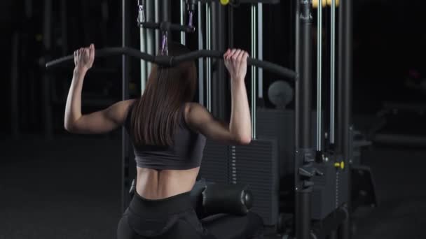 Mujer en el gimnasio levantamiento de bloques en la máquina de rack, entrenamiento de fuerza en el dispositivo de bloque, luz cinematográfica, vista trasera. — Vídeos de Stock