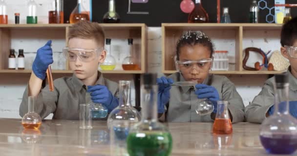 Laboratory experience in a chemistry lesson, kids in protective glasses pours a liquids into a flasks, modern education at school, children perform a chemical experiment, international school class. — Stock Video