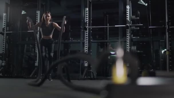 Здоровый образ жизни, женщина выполняет упражнения с боевыми канатами, выносливость тренировки в тренажерном зале, 4k замедленной съемки. — стоковое видео