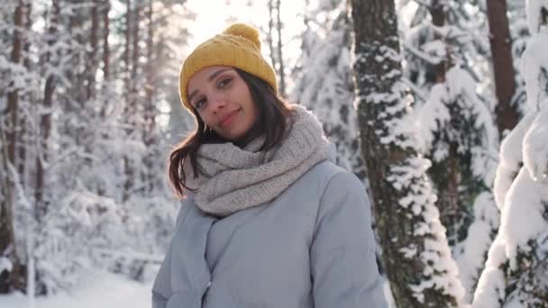 Kış ormanındaki güzel bir genç kızın portresi, neşeli bir kız doğadaki bir kış yürüyüşü sırasında poz veriyor ve kameraya bakıyor, 4k yavaş çekim.. — Stok video
