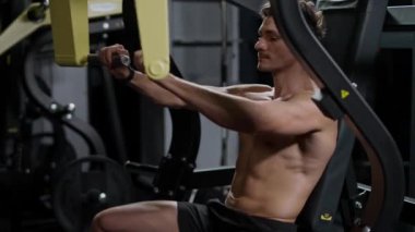 Spor salonundaki atletik adam jimnastik makinesindeki blokları kaldırıyor, blok aleti eğitimi alıyor, gece eğitimi alıyor, sinematik ışık alıyor..