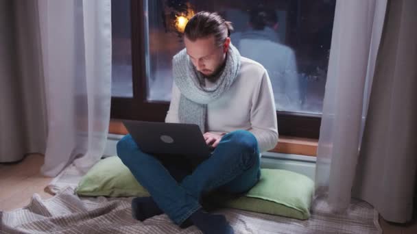 Man freelancer zit op de vloer en werkt aan een laptop, typt tekst op het toetsenbord, 's avonds tijd, werk op afstand van het landhuis, wintertijd. — Stockvideo