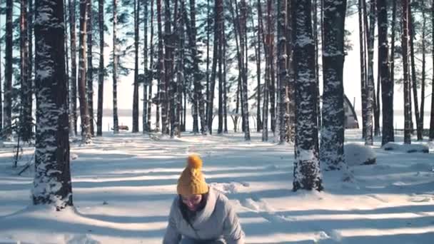 Retrato de una hermosa hembra joven en un bosque de invierno, una chica alegre lanza nieve y mirando a la cámara durante un paseo de invierno en la naturaleza, 4k cámara lenta. — Vídeos de Stock