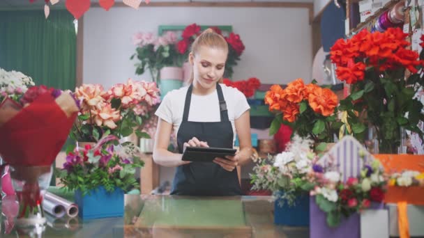 Botanica e lavorando con le piante, fiorista donna fa inventario in un negozio di fiori, una femmina utilizza una tavoletta schermo per contare il numero di fiori e piante in un negozio di fiori. — Video Stock