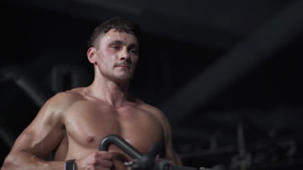 Hombre en el gimnasio levantamiento de bloques en la máquina de remo, entrenamiento en el dispositivo de bloque y equipo de gimnasio, entrenamiento nocturno, luz cinematográfica. — Vídeos de Stock