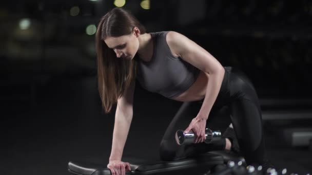Jonge vrouw in de sportschool, vrouw tilt een halter in een tilt, spiertraining met gewichten. — Stockvideo