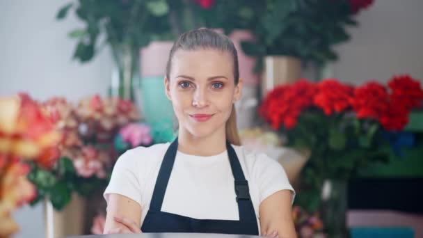 Portrait of young florist female, beautiful cheerful woman looks at the camera and smiles, the interior of a flower shop on the background, 4k slow motion. — Stock Video