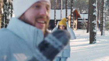 Kış ormanlarında genç ve neşeli bir çift, erkek ve dişi kamera önünde bir kış ormanının arka planında, güneşli kış havasında, erkek bir kızı kollarına alır..