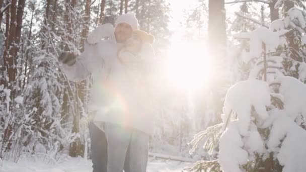 Jong koppel poseren op camera, man en vrouw nemen een selfie op een smartphone tegen de achtergrond van een winterbos, zonnig winterweer. — Stockvideo