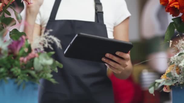 Florist kvinna tar inventering i en blomsteraffär, en hona använder en skärm tablett för att räkna antalet blommor och växter i en blomsteraffär. — Stockvideo