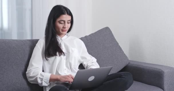 Vrouwelijke freelancer zit op de bank en werkt aan een laptop, typt tekst op het toetsenbord, 's avonds tijd, thuiswerk. — Stockvideo