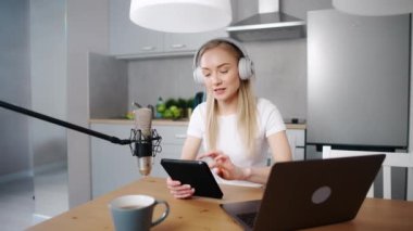 Kadın streamer sosyal ağlar için canlı bir podcast yapıyor, mutfakta otururken uzaktan çalışıyor, dizüstü bilgisayar ve tablet kullanıyor, koronavirüs salgını bağlamında çalışıyor, karantina.