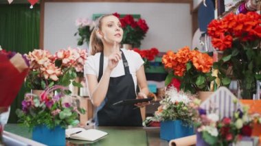 Botanik ve bitkilerle çalışan çiçekçi kadın çiçekçide envanter çıkarıyor. Bir kadın çiçekçi dükkanındaki çiçek ve bitkilerin sayısını saymak için ekran tableti kullanıyor..