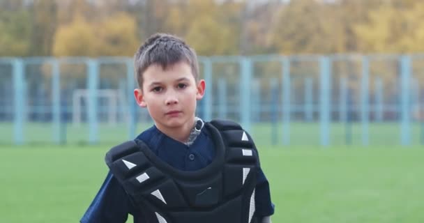 Porträtt av en pojke baseball spelare på en suddig bakgrund, sätter catcher på en skyddande hjälm och tittar på kameran, en allvarlig look, 4k slow motion. — Stockvideo