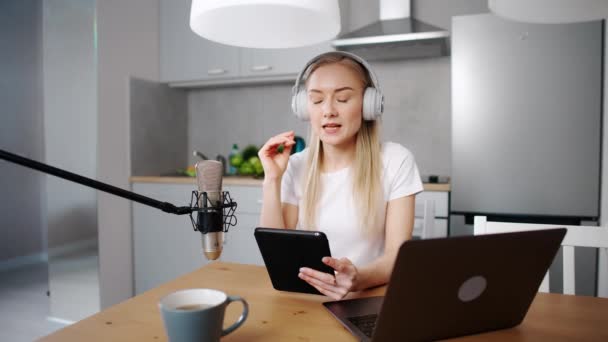 Kadın streamer sosyal ağlar için canlı bir podcast yapıyor, mutfakta otururken uzaktan çalışıyor, dizüstü bilgisayar ve tablet kullanıyor, koronavirüs salgını bağlamında çalışıyor, karantina. — Stok video