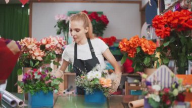 Neşeli kadın çiçekçi bir buket çiçeği bir kutuda süslüyor, genç bir kadın çiçekçide çalışıyor, çok renkli bir iç mekan..