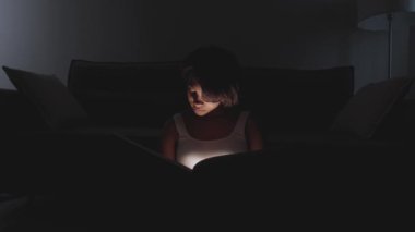 Evde oturup kitap okuyan genç bir kadının portresi, sıcak ışık, salgın sırasında kendini izole etme, mistik ışık efekti..