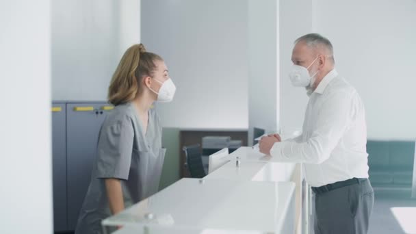 Recepción en el hospital, una enfermera registra a un paciente anciano para una cita con un médico en una clínica médica moderna, personas con máscaras médicas protectoras, pandemia de coronavirus. — Vídeos de Stock