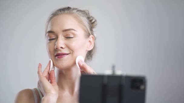 Retrato de blogger de belleza femenina, mujer muestra cómo masajear la cara con almohadillas de algodón, hace una corriente para las redes sociales en el teléfono inteligente, cuidado facial. — Vídeo de stock