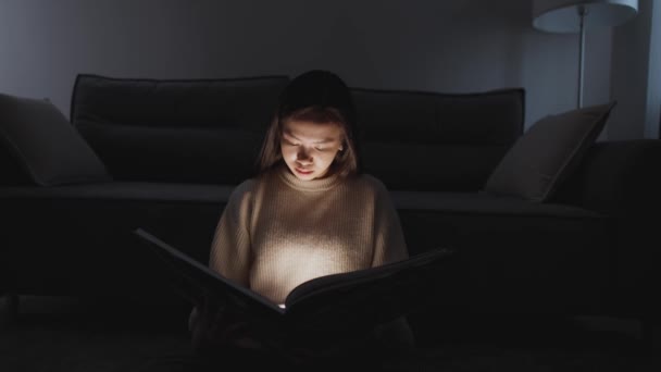 Noche, retrato de mujer asiática sentada en casa en el suelo y leyendo un libro, luz cálida, autoaislamiento durante la pandemia, efecto de iluminación mística. — Vídeos de Stock
