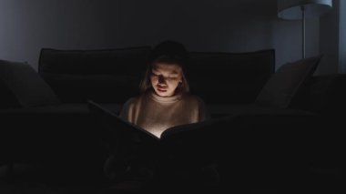 Gece vakti, evde oturup kitap okuyan Asyalı bir kadının portresi, sıcak ışık, salgın sırasında kendini izole etme, mistik ışık efekti..