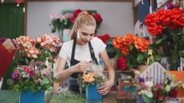 Neşeli bayan çiçekçi bir buket çiçeği bir kutuda süslüyor, neşeli bir kadın çiçekçide çalışıyor, çok renkli bir iç mekan..