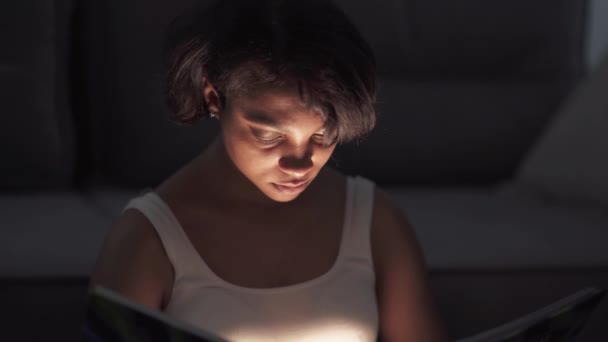 Портрет молодої жінки, яка сидить вдома на підлозі і читає книгу, тепле світло, самоізоляцію під час пандемії, ефект містичного освітлення . — стокове відео