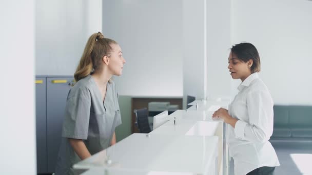 Nemocniční recepce, zdravotní sestra registruje mladou ženu pacienta na schůzku s lékařem v moderní lékařské klinice, lidé v ochranných lékařských maskách, koronavirová pandemie. — Stock video