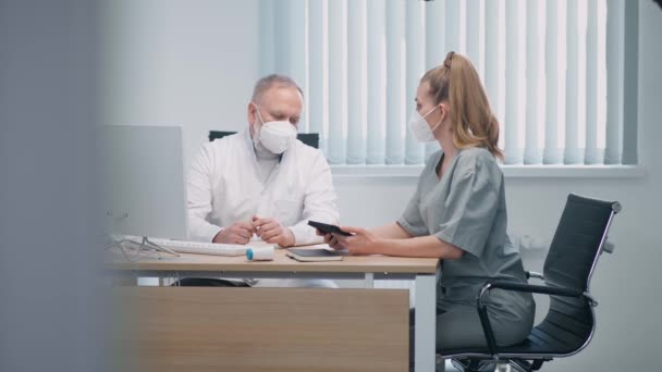 보호 마스크를 쓰고 있는 의료 전문가들은 환자를 치료하는 방법, 성인 남성 의사와 여성 간호사가 의학 문제에 대해 의사소통을 하고 스크린 태블릿을 사용하는 방법에 대해 토론 한다 — 비디오