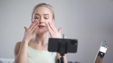 Kadın güzellik blogcusu portresi, kadın pamuk pedlerle nasıl masaj yapılacağını gösteriyor, akıllı telefondan sosyal ağlar için bir akış yaratıyor, yüz bakımı.