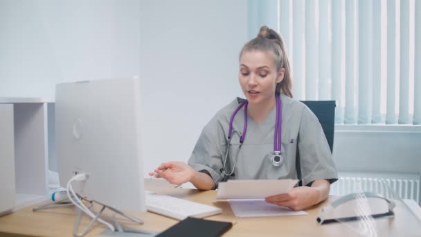 Γυναίκα γιατρός κάθεται στο χώρο εργασίας και επικοινωνεί με τον ασθενή μέσω βιντεοκλήσης, απομακρυσμένο συνέδριο των ιατρών και των ιατρών σε απευθείας σύνδεση, σύγχρονο νοσοκομείο. — Αρχείο Βίντεο