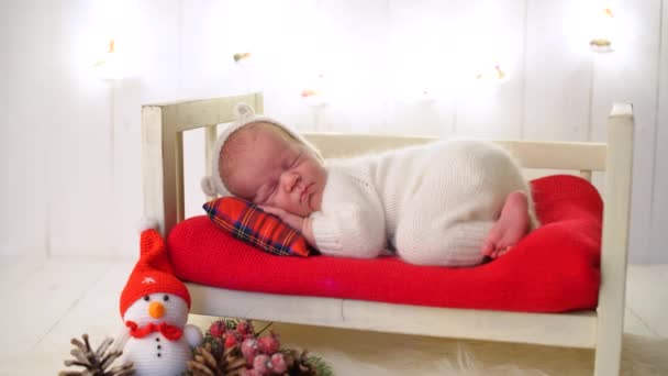 Bambino appena nato in pigiama bianco dorme tranquillamente su un lettino in un interno invernale, serenità e tranquillità, effetto sfocatura. — Video Stock