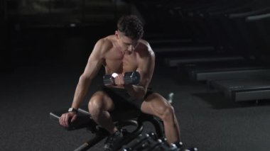 Sporcu adam spor salonunda antrenman yapıyor, dambılları kaldırıyor ve el egzersizleri yapıyor, bir atlet spor salonunda pazılarını çalıştırıyor, sinematik ışık, 4 km yavaş çekim..