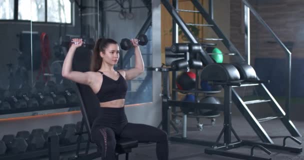 Jonge vrouwelijke training in de Gym, meisje tilt haltergewichten op de bank, spiertraining met gewichten, 4k 50fps. — Stockvideo