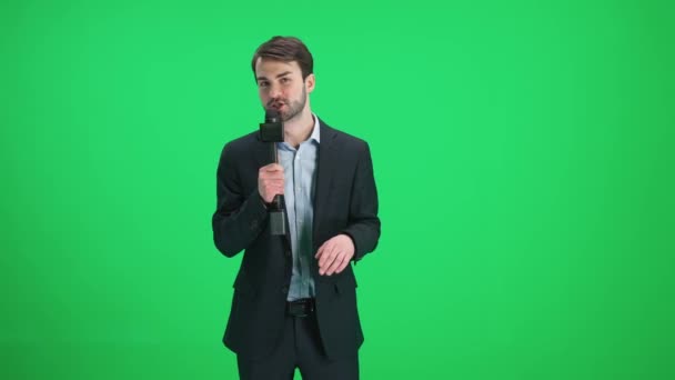 Muž reportér v obleku se podívá do kamery a mluví do mikrofonu na zeleném pozadí, šablony pro televizní zpravodajské agentury, novinář v práci, chromakey. — Stock video