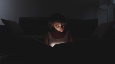 Evde oturup kitap okuyan genç bir kadının portresi, sıcak ışık, salgın sırasında kendini izole etme, mistik ışık efekti..