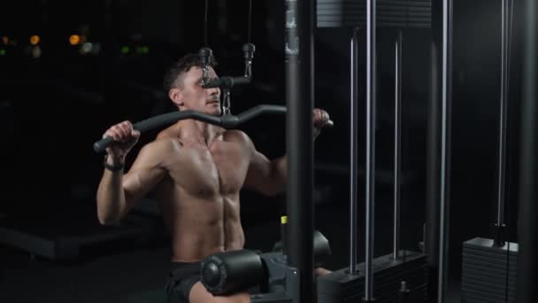 Homem atlético na academia levantando blocos na máquina de rack, treinamento em dispositivo de bloco e equipamentos de ginástica, noite, câmera lenta 4k. — Vídeo de Stock