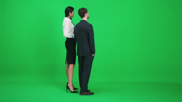 Några unga människor i kostym, man och kvinna står i grönområdet i chromakey, titta på och diskutera enkla saker, en mall på en grön bakgrund, baksida visa. — Stockvideo
