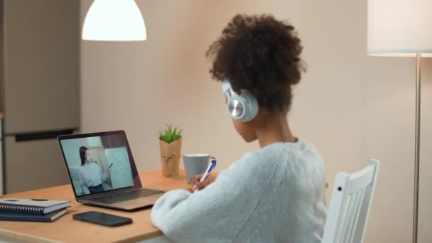 Молода африканська дівчина сидить за столом і навчається онлайн за допомогою ноутбука, школярка вчиться на віддаленому уроці за допомогою відеозв'язку з вчителем, навчання в умовах пандемії коронавірусу — стокове відео