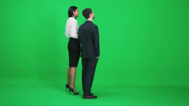 Homem e mulher de terno fica no espaço verde do chromakey, eles discutem assuntos enquanto olham na frente deles, um modelo em um fundo verde, visão traseira. — Vídeo de Stock