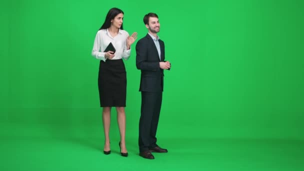 Homem e mulher de terno fica no espaço verde do chromakey, eles discutem assuntos enquanto olham na frente deles, um modelo em um fundo verde. — Vídeo de Stock