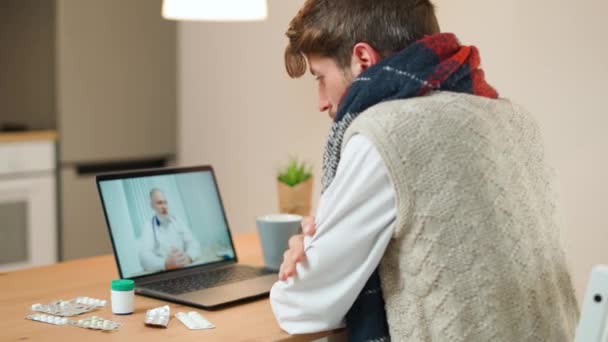 El hombre en aislamiento se comunica con un médico por videollamada usando una computadora portátil, un paciente consulta a un médico en línea mientras está en cuarentena, una pandemia de coronovirus. — Vídeos de Stock