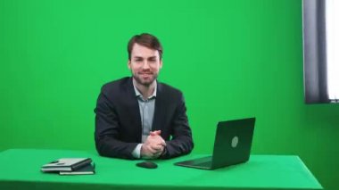 Takım elbiseli bir muhabir stüdyoda oturur ve kameraya bakar, konuşur ve sunar bir haber programı yeşil bir arka plan, TV haber ajansları için bir şablon, iş yerinde bir gazeteci, kromakey.