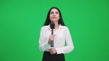 Takım elbiseli kadın muhabir kameraya bakar ve yeşil arka planda bir mikrofona konuşur, TV haber ajansları için bir şablon, iş yerinde bir gazeteci, kromakey.