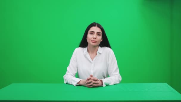 Mulher repórter de terno senta-se no estúdio e olha para a câmera, fala e hospeda um programa de notícias em um fundo verde, um modelo para agências de notícias de TV, jornalista no trabalho, chromakey. — Vídeo de Stock