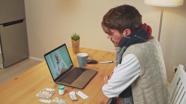 Sjuk man i självisolering kommunicerar med en läkare genom videosamtal med hjälp av en bärbar dator, en patient konsulterar en läkare online medan i karantän, en coronovirus pandemi. — Stockvideo