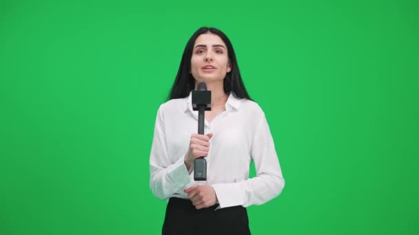 Vrouw verslaggever in pak kijkt in de camera en spreekt in een microfoon op een groene achtergrond, een sjabloon voor tv-nieuwsagentschappen, journalist op het werk, chromakey. — Stockvideo